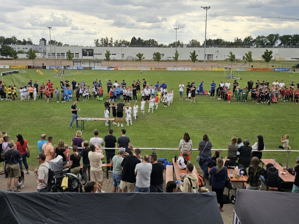 Gruppierung von Kindern in Fußballtrikots bei einer Veranstaltung auf einem Sportplatz.