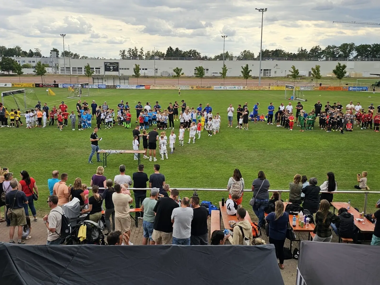 Gruppierung von Kindern in Fußballtrikots bei einer Veranstaltung auf einem Sportplatz.