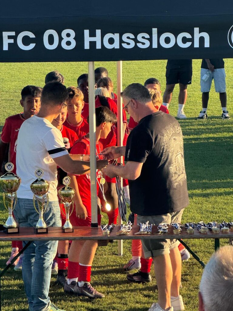Ein Trainer überreicht einem jungen Spieler einen Pokal bei einer Zeremonie des FC 08 Hassloch.