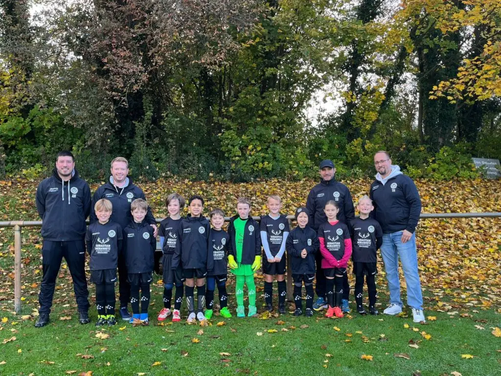 Eine Jugendfußballmannschaft in schwarzen Trikots steht mit ihren Trainern auf einem Sportplatz.