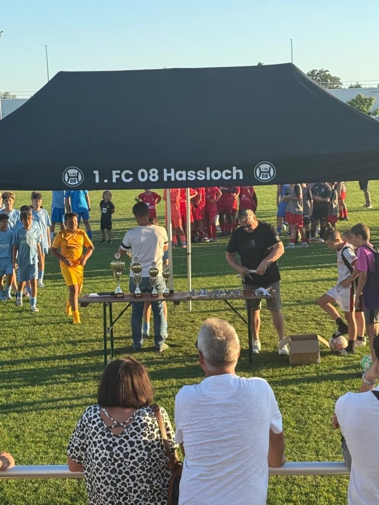 Menschen versammeln sich unter einem Zelt des 1. FC 08 Hassloch bei einer Sportveranstaltung mit Pokalen.