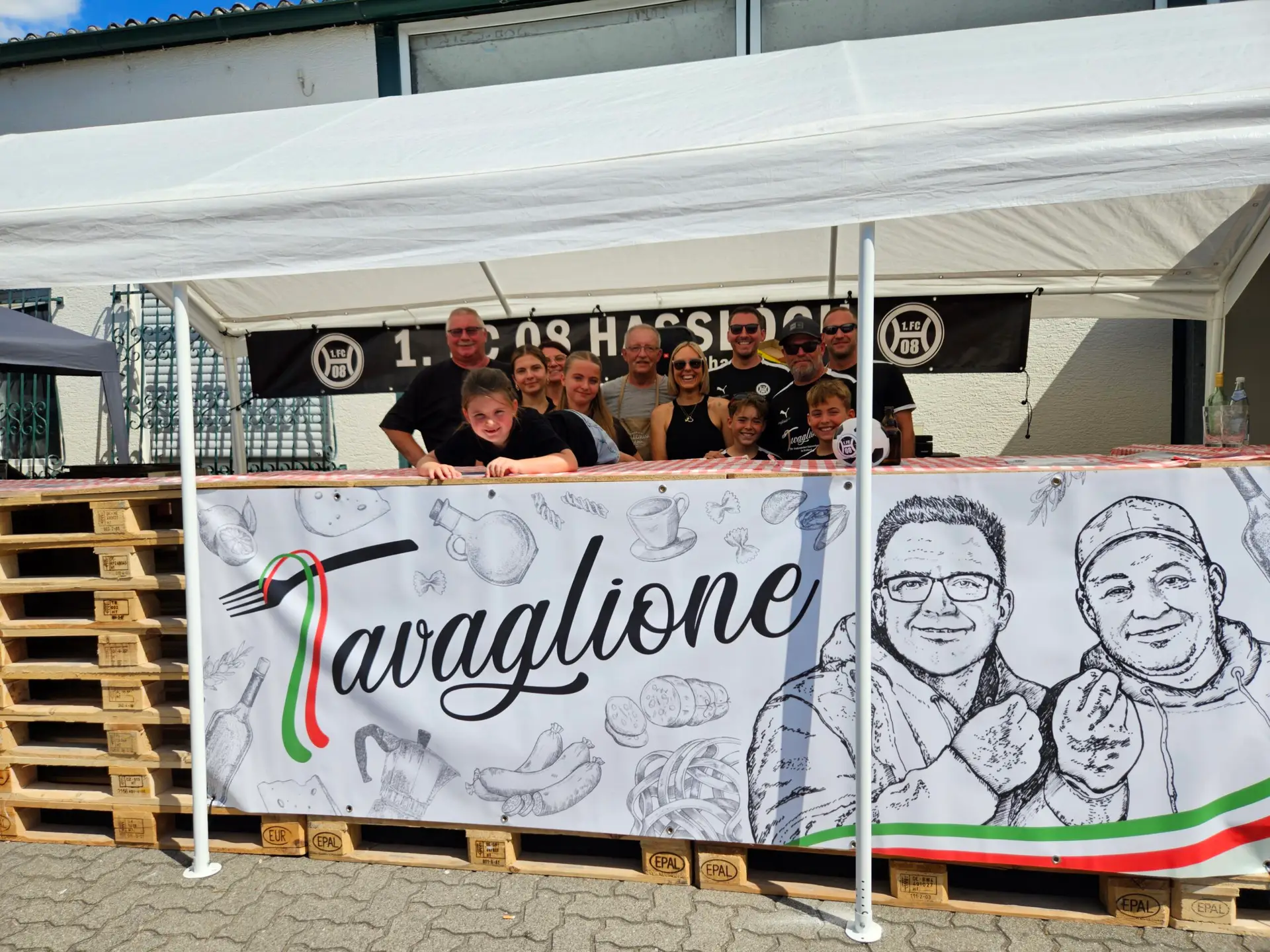 Ein Team von Personen steht hinter einem Food Stand mit einem Banner, das den Namen Tavaglione zeigt.