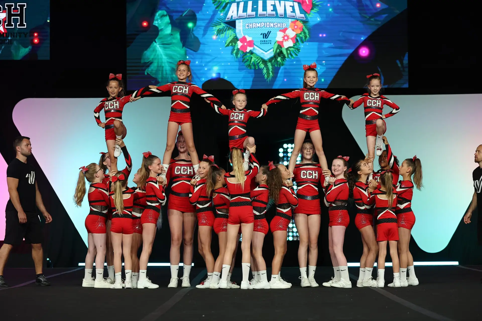 Cheerleading-Team in roten und schwarzen Uniformen führt eine Gruppenakrobatik auf einer Bühne durch.