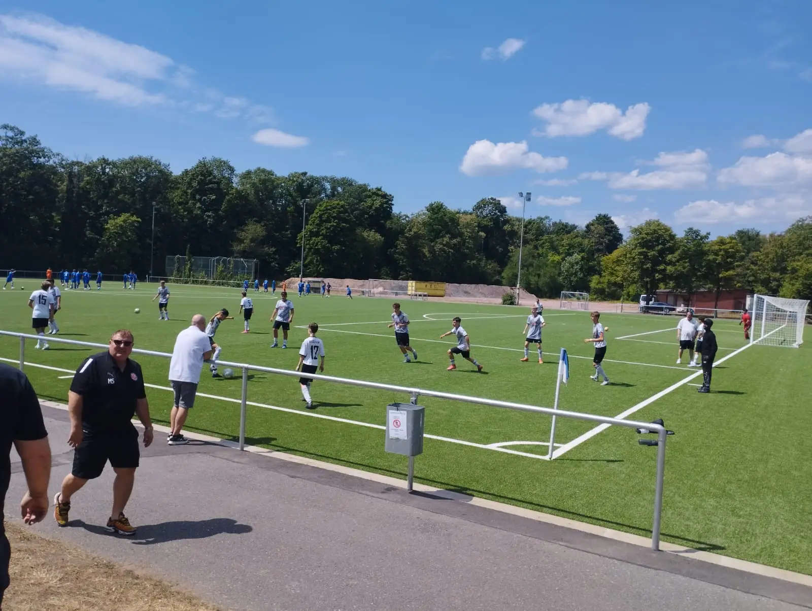 Gruppen von Spielern, die auf einem Kunstrasenplatz Fußball trainieren, mit Toren im Hintergrund.