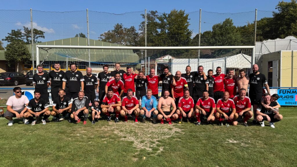Gruppenfoto von Spielern einer Fußballmannschaft in roten Trikots auf einem Sportplatz.