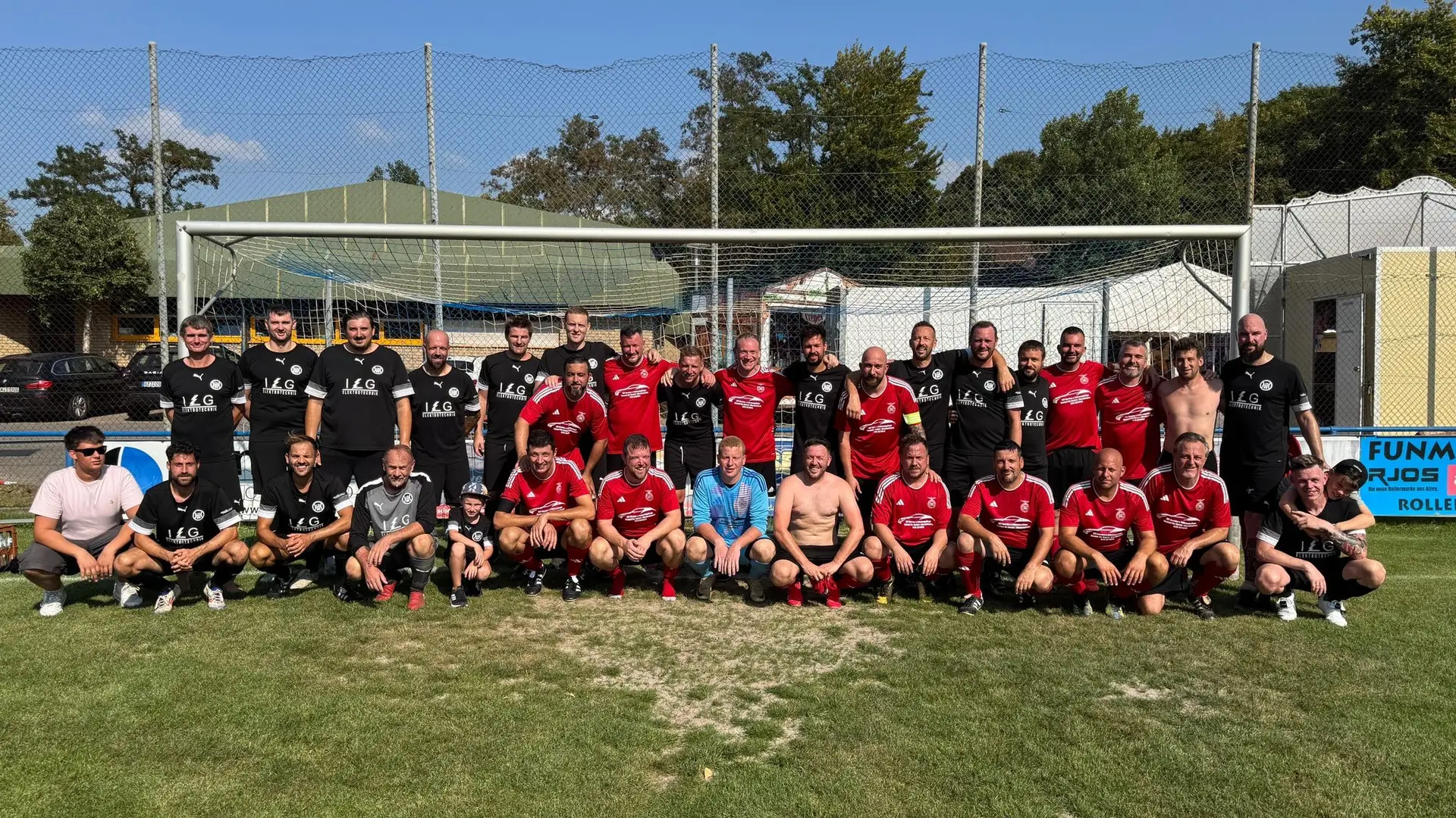 Gruppenfoto von Spielern einer Fußballmannschaft in roten Trikots auf einem Sportplatz.