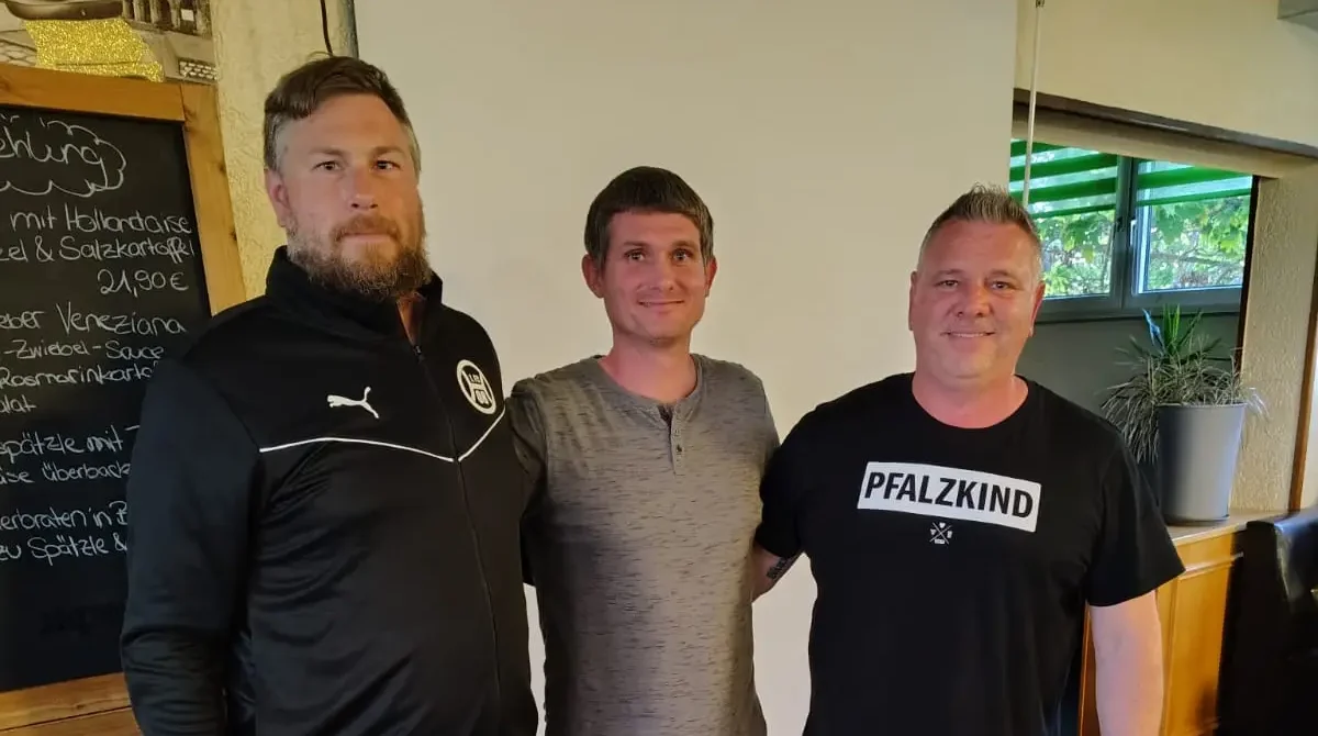 Drei Personen stehen nebeneinander in einem Raum, zwei Männer tragen Sportbekleidung und einer trägt ein schwarzes T-Shirt.