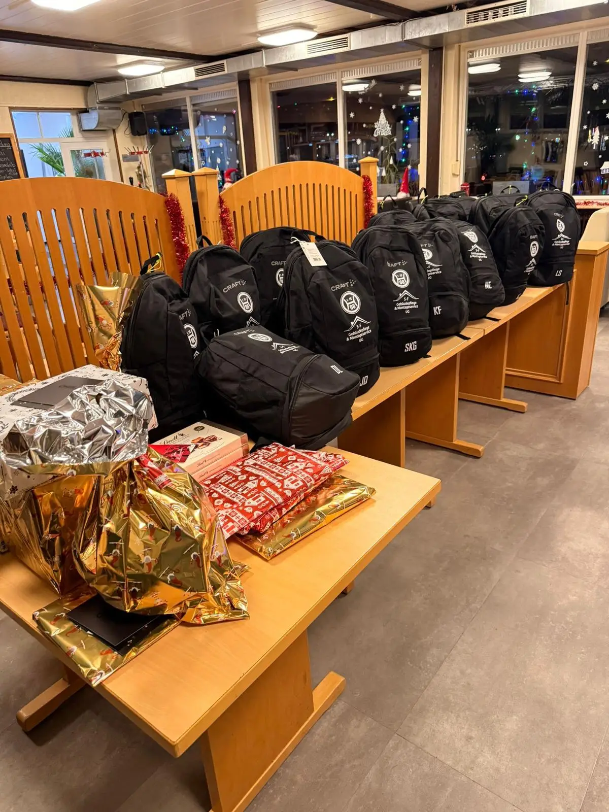 Reihe von schwarzen Sporttaschen mit Logos auf einem Tisch in einem Innenraum.