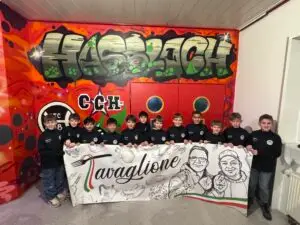 Gruppe von Kindern in schwarzen Jacken, die ein Banner mit Zeichnungen und Text halten.