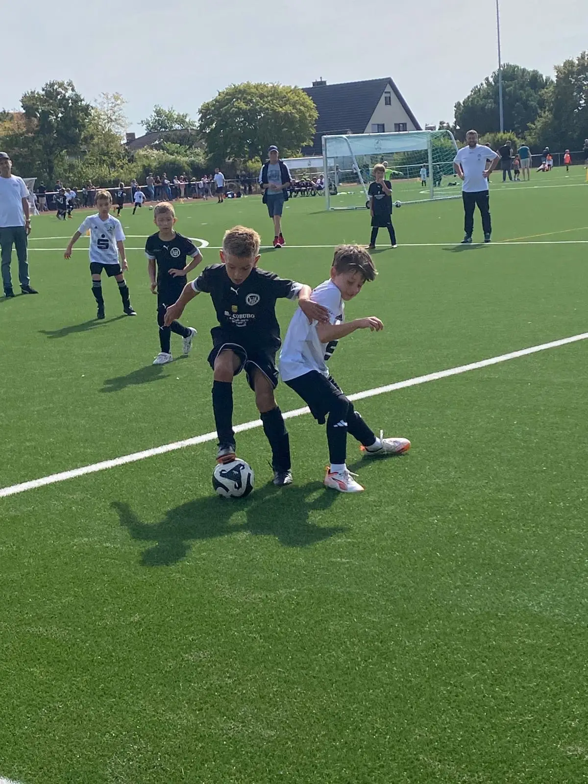 Zwei Kinder im Fußballtrikot kämpfen um den Ball auf einem Kunstrasenplatz während eines Spiels.
