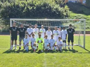 Eine Fußballmannschaft mit Trainern steht vor einem Tor auf dem Spielfeld in weißen Trikots.