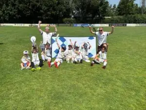Eine Gruppe von Kindern und Trainern posiert auf einem Sportplatz, alle mit Medaillen und einem Banner.