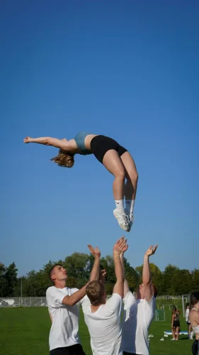 Eine Person wird von mehreren Menschen in die Luft geworfen, während sie einen Rückwärtssalto ausführt.