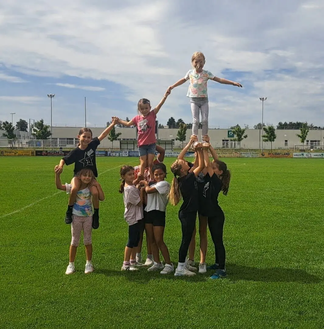 Eine Gruppe von Kindern, die eine Menschenpyramide auf einem Sportfeld bildet.